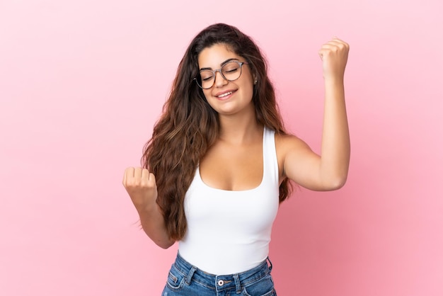 Young caucasian woman isolated on pink background celebrating a victory