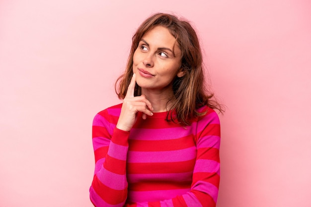 Photo young caucasian woman isolated on pink background contemplating planning a strategy thinking about the way of a business