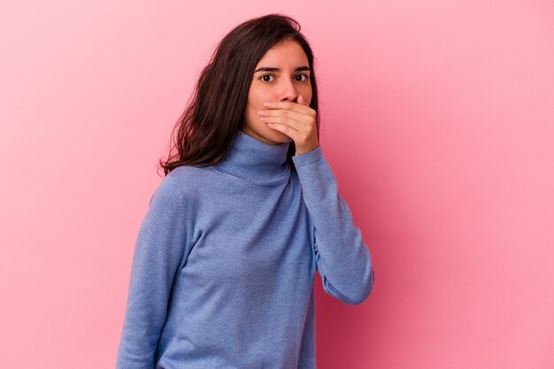 Young caucasian woman isolated on pink background covering mouth with hands looking worried.