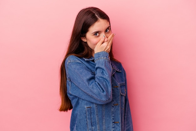 Young caucasian woman isolated on pink background covering mouth with hands looking worried.