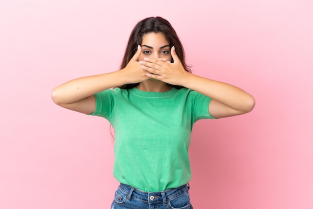 Young caucasian woman isolated on pink background covering mouth with hands