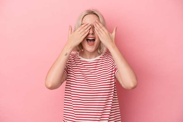 Photo young caucasian woman isolated on pink background covers eyes with hands smiles broadly waiting for a surprise