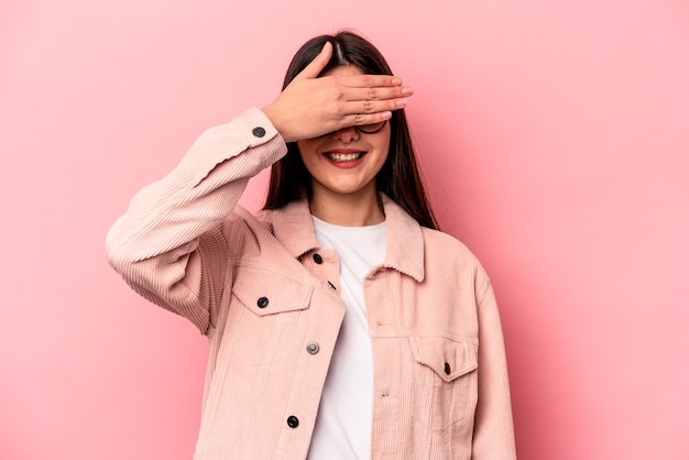 Young caucasian woman isolated on pink background covers eyes with hands smiles broadly waiting for a surprise