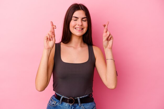 Young caucasian woman isolated on pink background crossing fingers for having luck