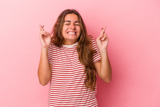 Young caucasian woman isolated on pink background  crossing fingers for having luck