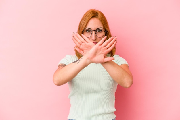 拒否ジェスチャーをしているピンクの背景に分離された若い白人女性