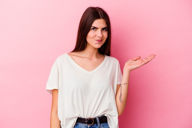 Young caucasian woman isolated on pink background doubting and shrugging shoulders in questioning gesture.