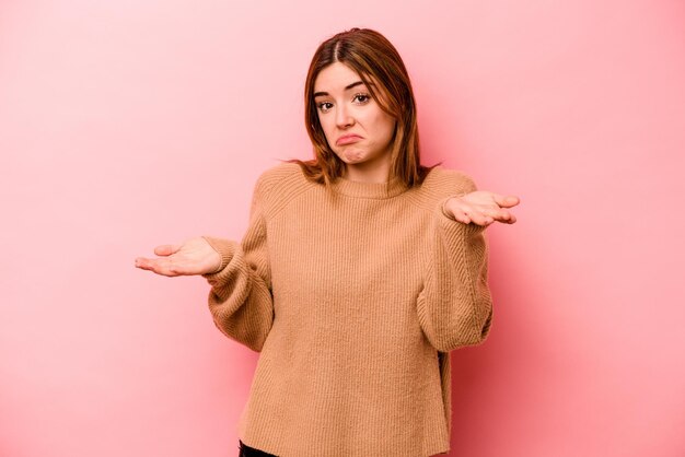 Young caucasian woman isolated on pink background doubting and shrugging shoulders in questioning gesture