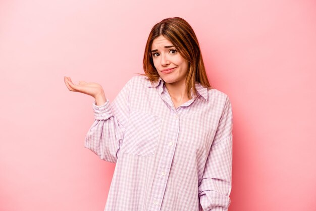Young caucasian woman isolated on pink background doubting and shrugging shoulders in questioning gesture