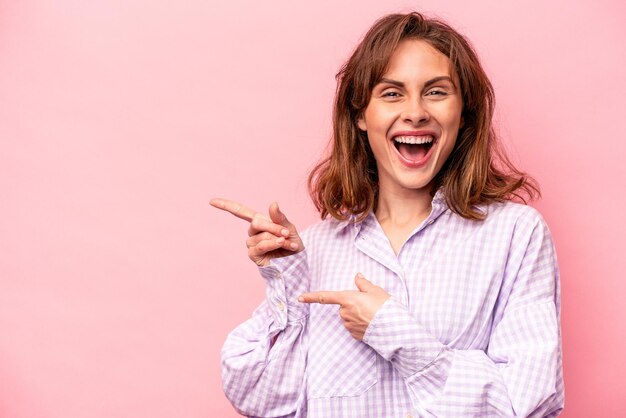 Young caucasian woman isolated on pink background excited pointing with forefingers away