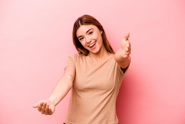 Young caucasian woman isolated on pink background feels confident giving a hug to the camera