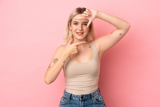 Young caucasian woman isolated on pink background focusing face. Framing symbol