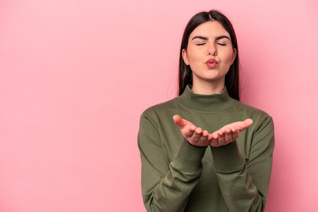 Foto giovane donna caucasica isolata su sfondo rosa che piega le labbra e tiene i palmi delle mani per inviare un bacio d'aria