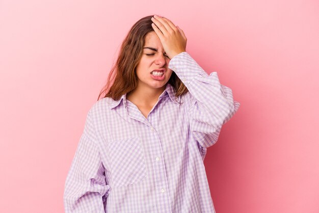 Young caucasian woman isolated on pink background  forgetting something, slapping forehead with palm and closing eyes.