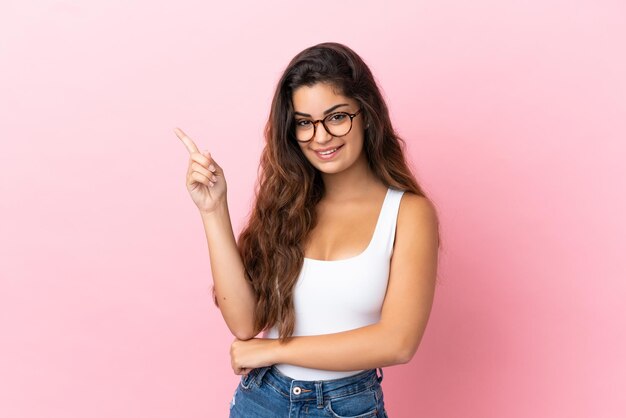 Young caucasian woman isolated on pink background happy and pointing up