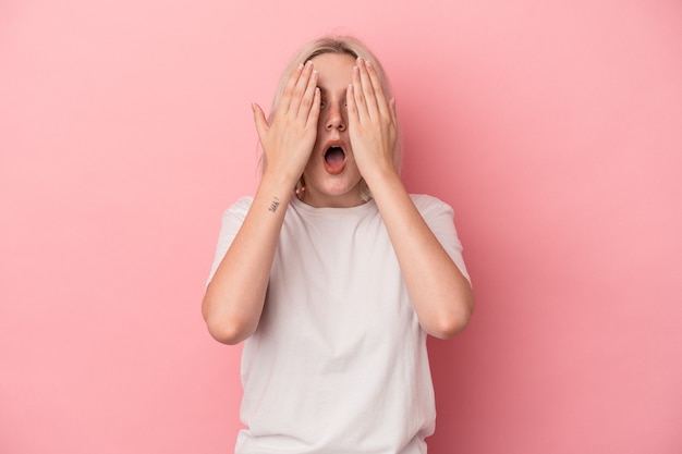 Young caucasian woman isolated on pink background having fun covering half of face with palm.