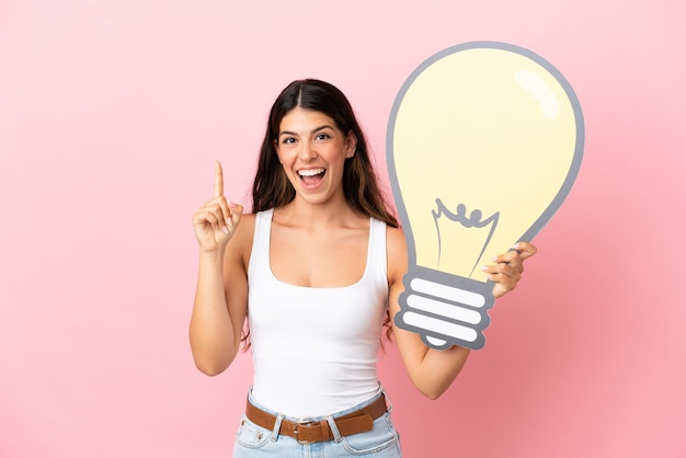 Foto giovane donna caucasica isolata su sfondo rosa con in mano un'icona a forma di lampadina e pensiero