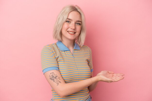 Young caucasian woman isolated on pink background holding a copy space on a palm.