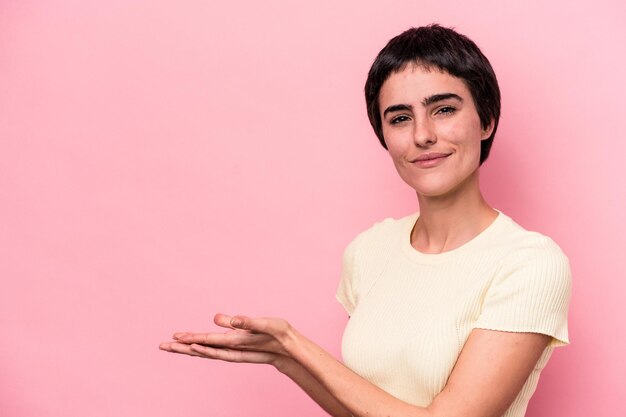 Young caucasian woman isolated on pink background holding a copy space on a palm.