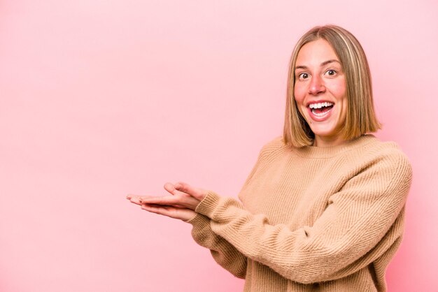 Young caucasian woman isolated on pink background holding a copy space on a palm