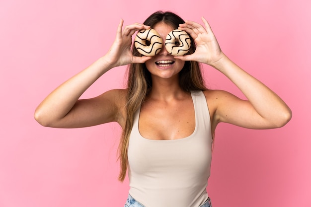 Young caucasian woman isolated on pink background holding donuts in an eye