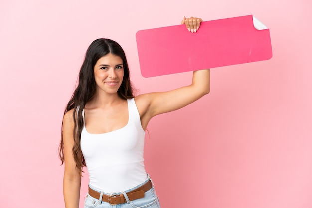 Young caucasian woman isolated on pink background holding an empty placard