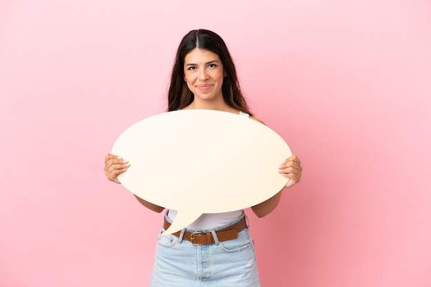 Young caucasian woman isolated on pink background holding an empty speech bubble