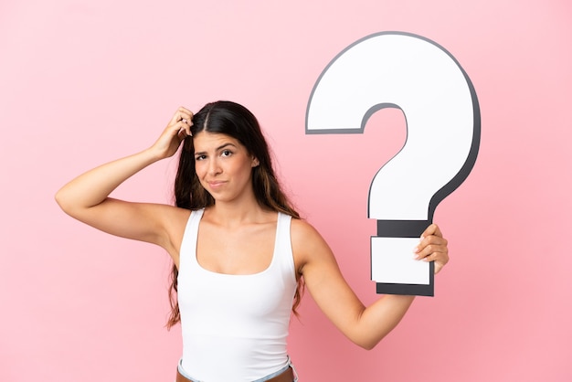 Young caucasian woman isolated on pink background holding a question mark icon and having doubts