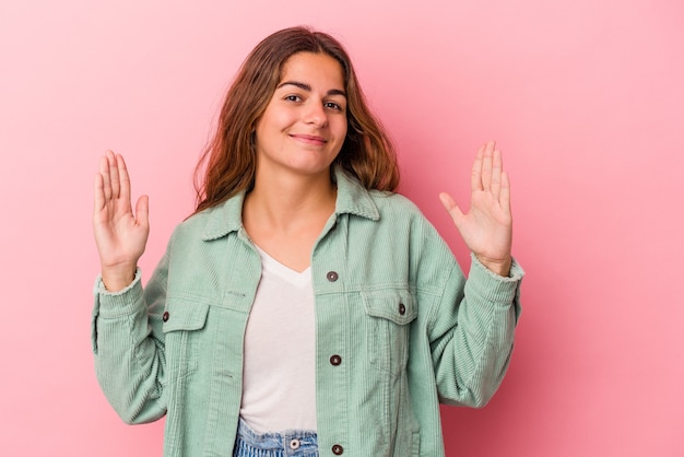 Foto giovane donna caucasica isolata su sfondo rosa che tiene qualcosa di piccolo con l'indice, sorridente e sicura di sé.