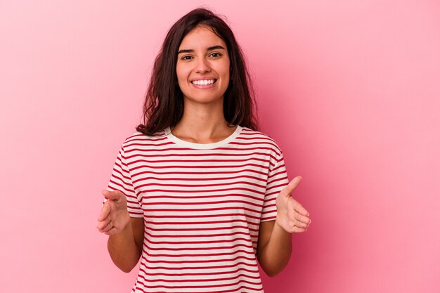 Young caucasian woman isolated on pink background holding something with both hands, product presentation.