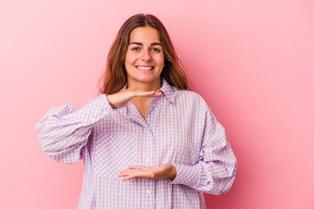 Young caucasian woman isolated on pink background  holding something with both hands, product presentation.