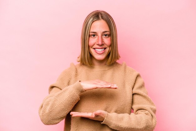 両手で何かを保持しているピンクの背景に分離された若い白人女性製品プレゼンテーション