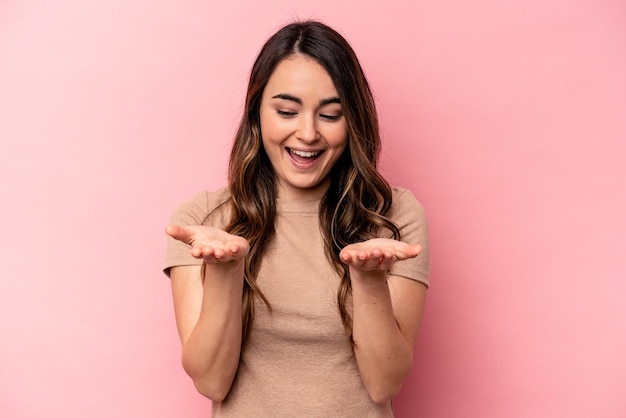 Young caucasian woman isolated on pink background holding something with palms offering to camera