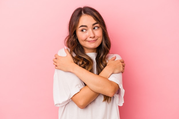 Young caucasian woman isolated on pink background hugs, smiling carefree and happy.