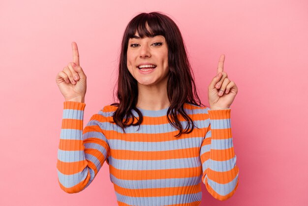 Young caucasian woman isolated on pink background indicates with both fore fingers up showing a blank space.