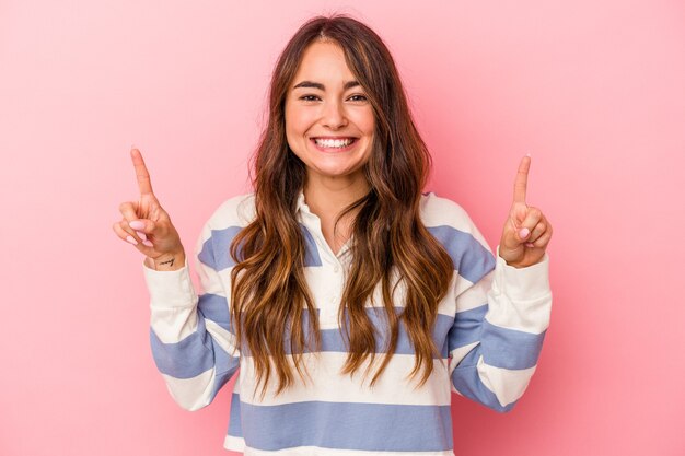 Young caucasian woman isolated on pink background indicates with both fore fingers up showing a blank space.