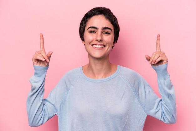 Young caucasian woman isolated on pink background indicates with both fore fingers up showing a blank space.