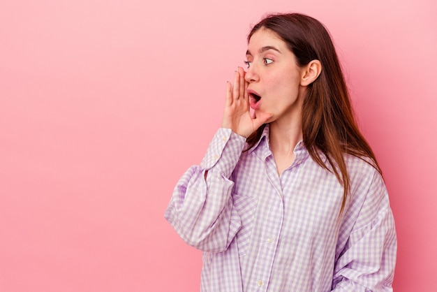 Young caucasian woman isolated on pink background is saying a secret hot braking news and looking aside