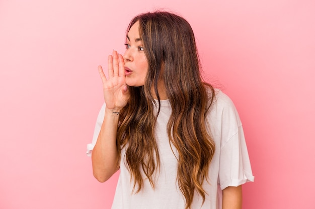 Young caucasian woman isolated on pink background is saying a secret hot braking news and looking aside