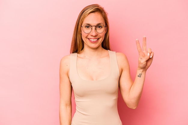 Young caucasian woman isolated on pink background joyful and carefree showing a peace symbol with fingers