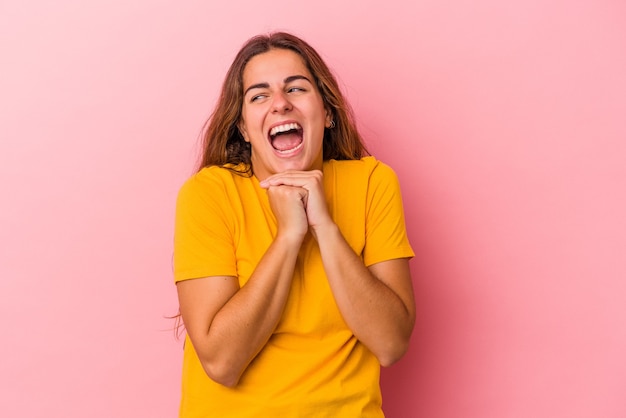 Young caucasian woman isolated on pink background  keeps hands under chin, is looking happily aside.