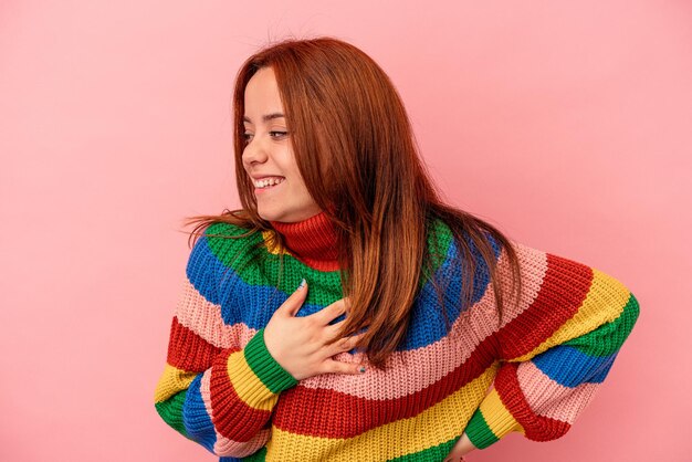 Young caucasian woman isolated on pink background laughing keeping hands on heart, concept of happiness.