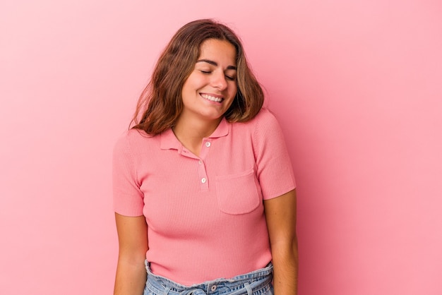 Young caucasian woman isolated on pink background  laughs and closes eyes, feels relaxed and happy.