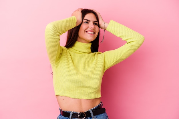 Young caucasian woman isolated on pink background laughs joyfully keeping hands on head. Happiness concept.