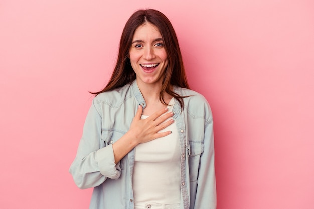 Young caucasian woman isolated on pink background laughs out loudly keeping hand on chest.