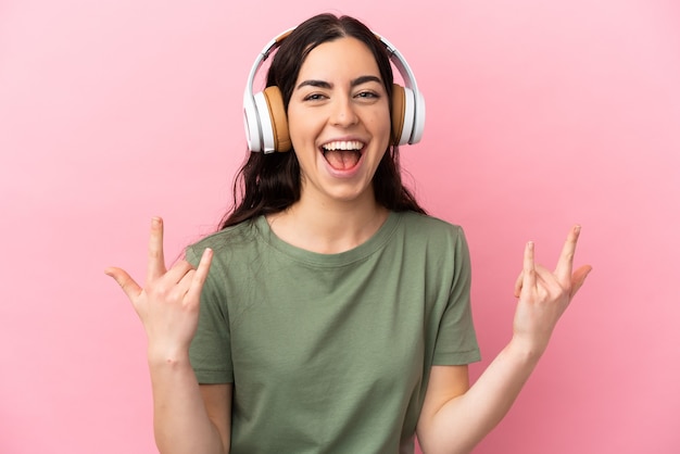 Young caucasian woman isolated on pink background listening music making rock gesture