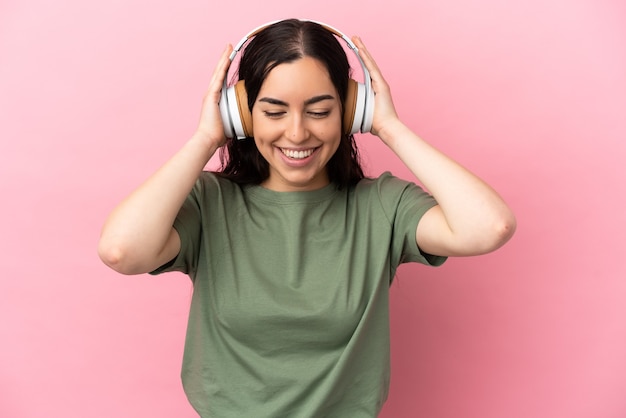 Giovane donna caucasica isolata su sfondo rosa ascoltando musica