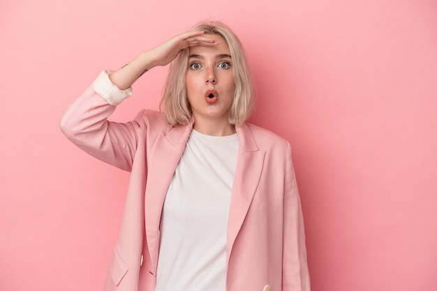 Young caucasian woman isolated on pink background looking far away keeping hand on forehead.