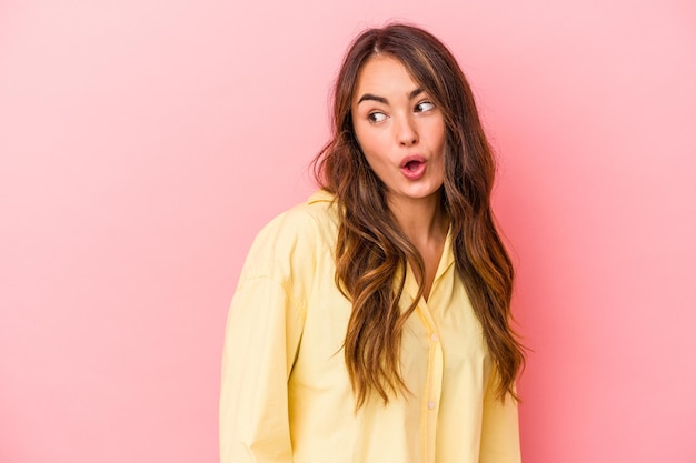 Young caucasian woman isolated on pink background looks aside smiling, cheerful and pleasant.