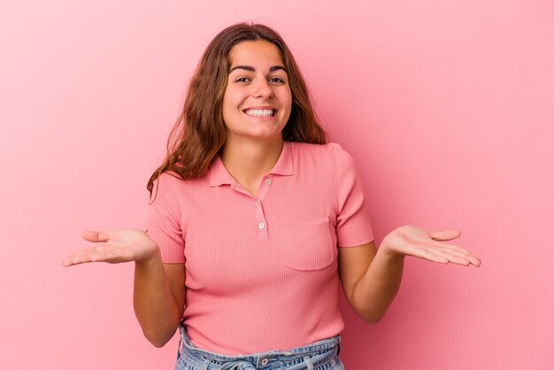 Young caucasian woman isolated on pink background  makes scale with arms, feels happy and confident.